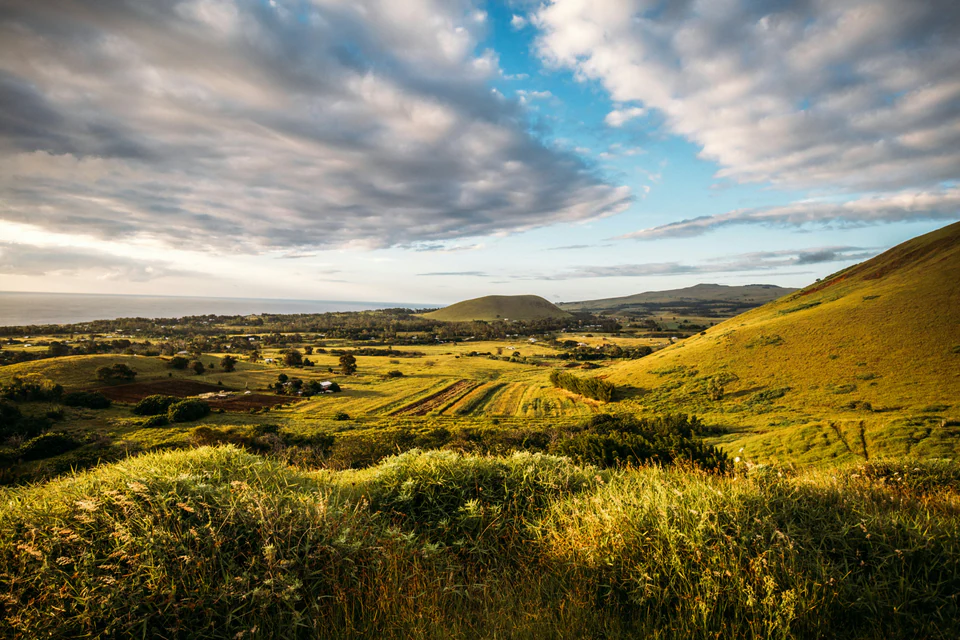 Sunlit farmland and rolling green hills beneath a cloud-filled sky