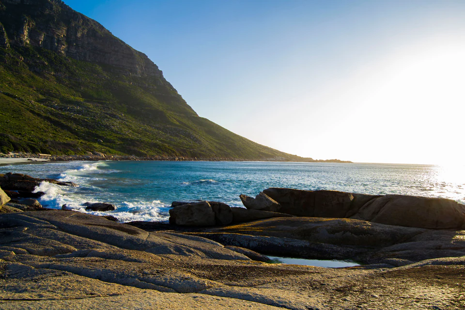 Rocky shoreline and a mountain slope beside a sunlit bay